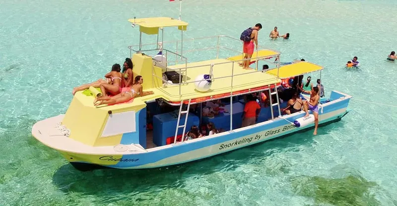 A glass-bottom boat above three reefs with tropical fish visible below on a VIP Cozumel snorkeling tour